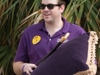 A male student wearing a purple shit holds a gold cane and a purple pillow