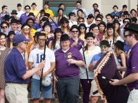 A male student wearing a purple shit hands a gold cane to another man
