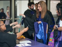 A female student holds graduation attire and talks to a woman at a table