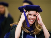 A female student wears a graduation robe and cap and smiles