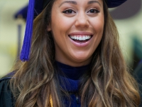 A female student wears a graduation robe and cap and smiles