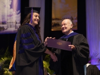 A man hands a student wearing graduation attire a diploma