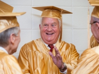 A man wearing a gold graduation cap and gown smiles