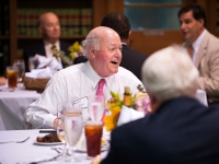 A man wearing a suit and tie is seated at a table and smiles