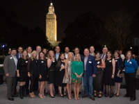 A group of people pose for a photo with the Louisiana state capitol in the background.