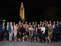 A group of people pose for a photo with the Louisiana state capitol in the background.