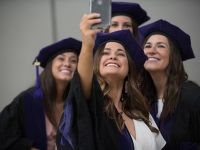 Two female students wearing graduation attire take a selfie