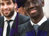 A male student wears a graduation robe and cap and smiles