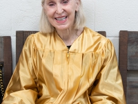 A woman wearing a gold robe smiles for a photo
