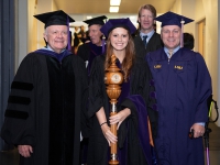 A female student wearing graduation attire holds a wooden mace