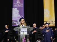 A female student wearing graduation attire sings at a podium