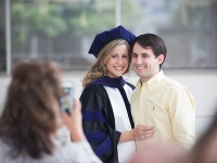 A female student wearing graduation attire smiles for a photo with a male