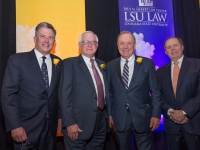A group photo of four men wearing semi-formal attire with purple and gold banners in the background