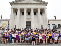 A woman talks on a microphone with a group of people behind him on the steps of the LSU Law Center
