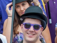 A man wearing a derby hat and sunglasses smiles