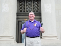 A man smiles while holding a black and gold cane