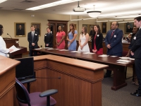 Nine students wearing business attire stand behind a table