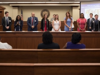 Nine students wearing business attire stand and face a seated audience