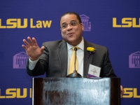 A man in a suit and tie talks at a podium with the LSU Law logo in the background