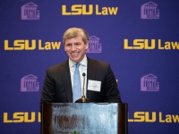A man in a suit and tie talks at a podium with the LSU Law logo in the background