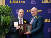 Two men wearing suits and ties hold a wooden plaque and smile for a photo