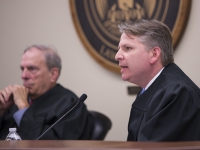 A man in judges robes speaks with another judge in the background