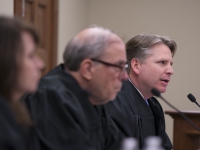A man in judges robes speaks with two other judges in the foreground