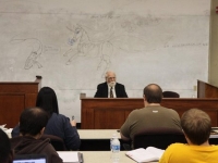 A male professor sits at the front of a classroom