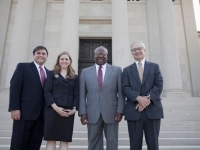 Three men and a woman wearing suits stand outside the front of the LSU Law Center