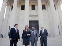 Three men and a woman wearing suits talk outside the front of the LSU Law Center