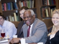 A man wearing a suit and tie laughs as he sits at a table