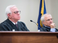 Two men wearing judges robes sit and look on