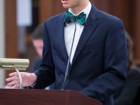 A male student wearing a suit and tie speaks at a podium